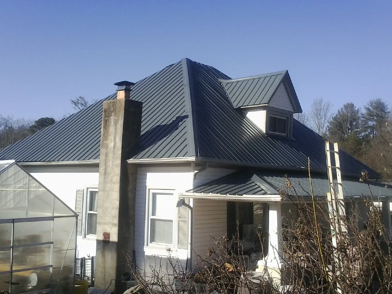 Dark blue standing seam metal roof on a white farmhouse with dormer — Slate & Tile Roof Repair by Roofing Brothers in Terra Alta