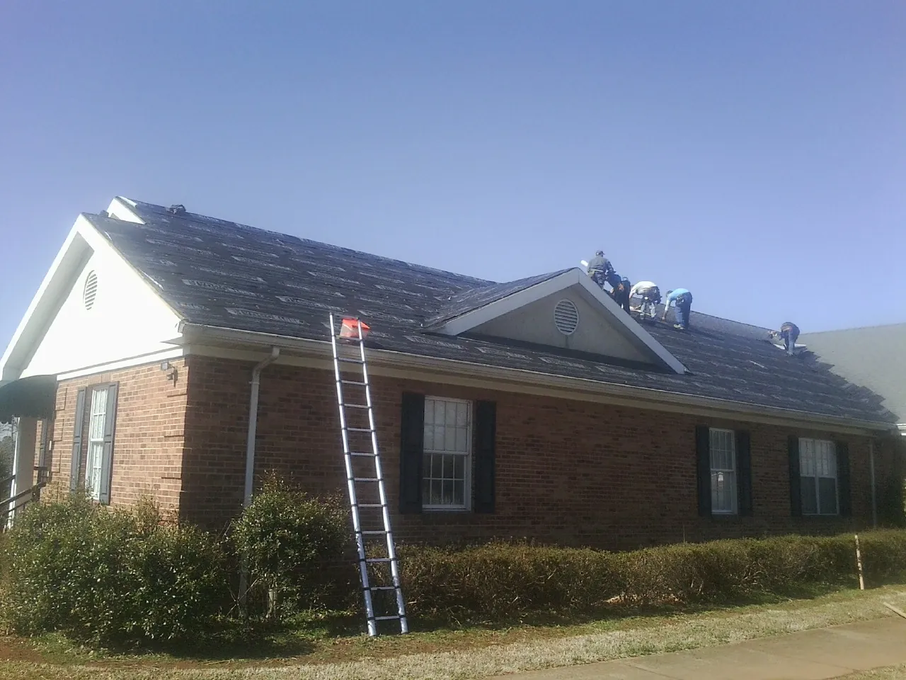 Crew tearing shingles off a brick ranch roof with a ladder set — Emergency Roof Repair work by our crew in Terra Alta