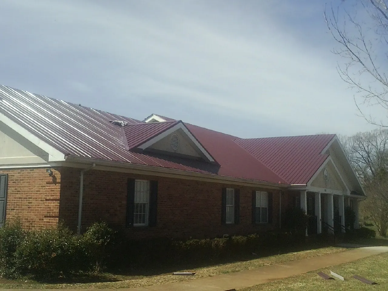 Red metal roof with gabled entries on a long brick building, from a Hail Damage Roof Repair job in Terra Alta
