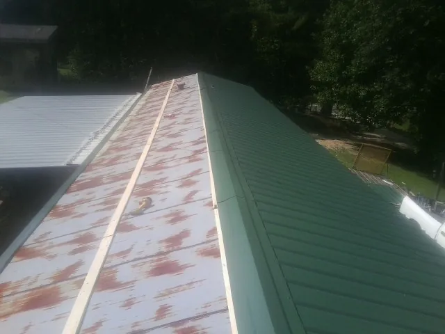 Old rusted panels beside newly installed green metal roofing — Wind Damage Roof Repair by Roofing Brothers in Terra Alta