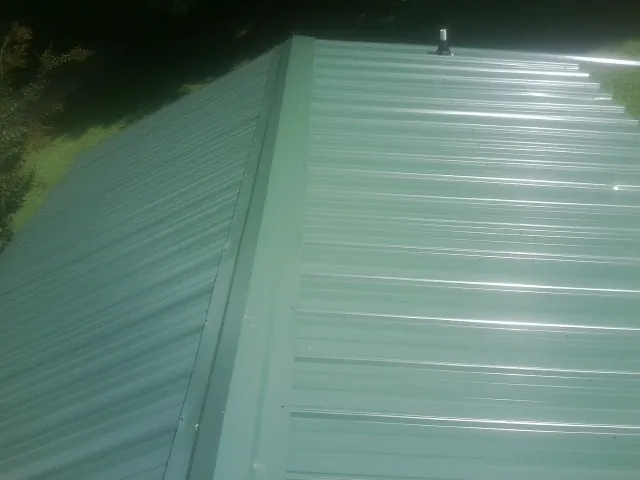 New green metal panels meeting at the ridge of a roof — Flat Roof Repair work by our crew in Terra Alta