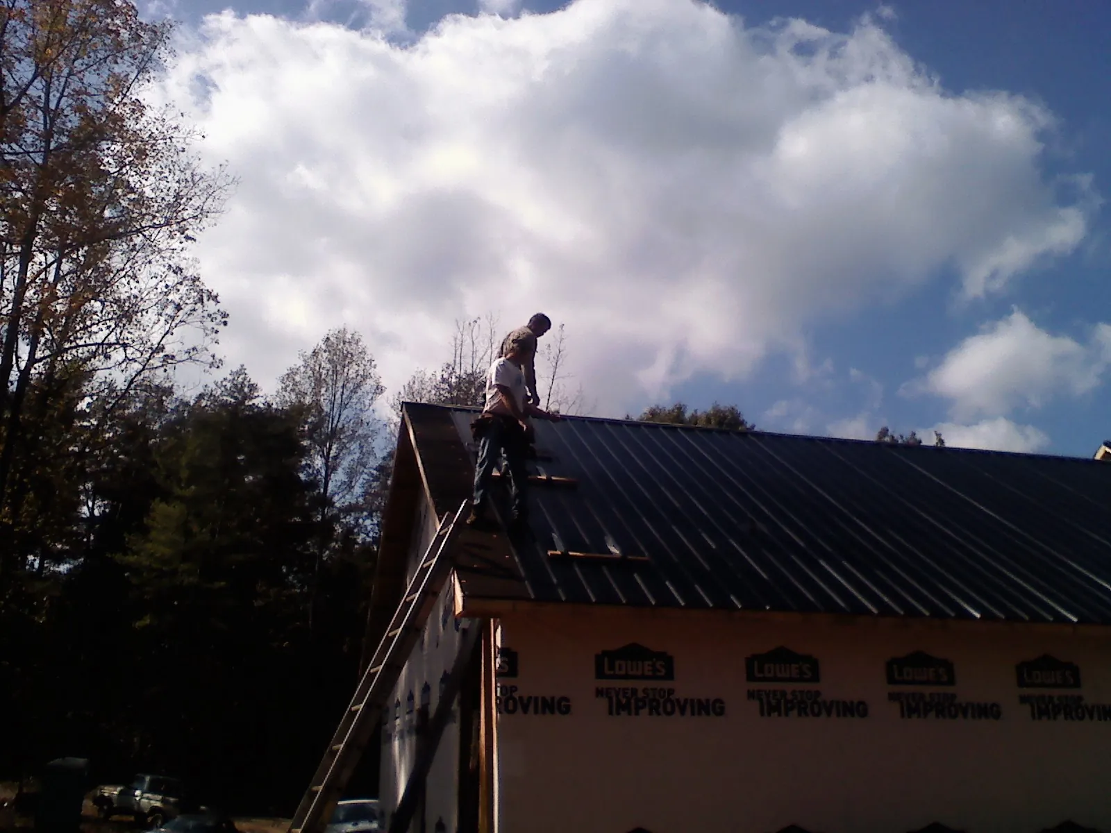Roofer fastening dark metal panels high against a cloudy sky, from a Roof Inspection job in Terra Alta