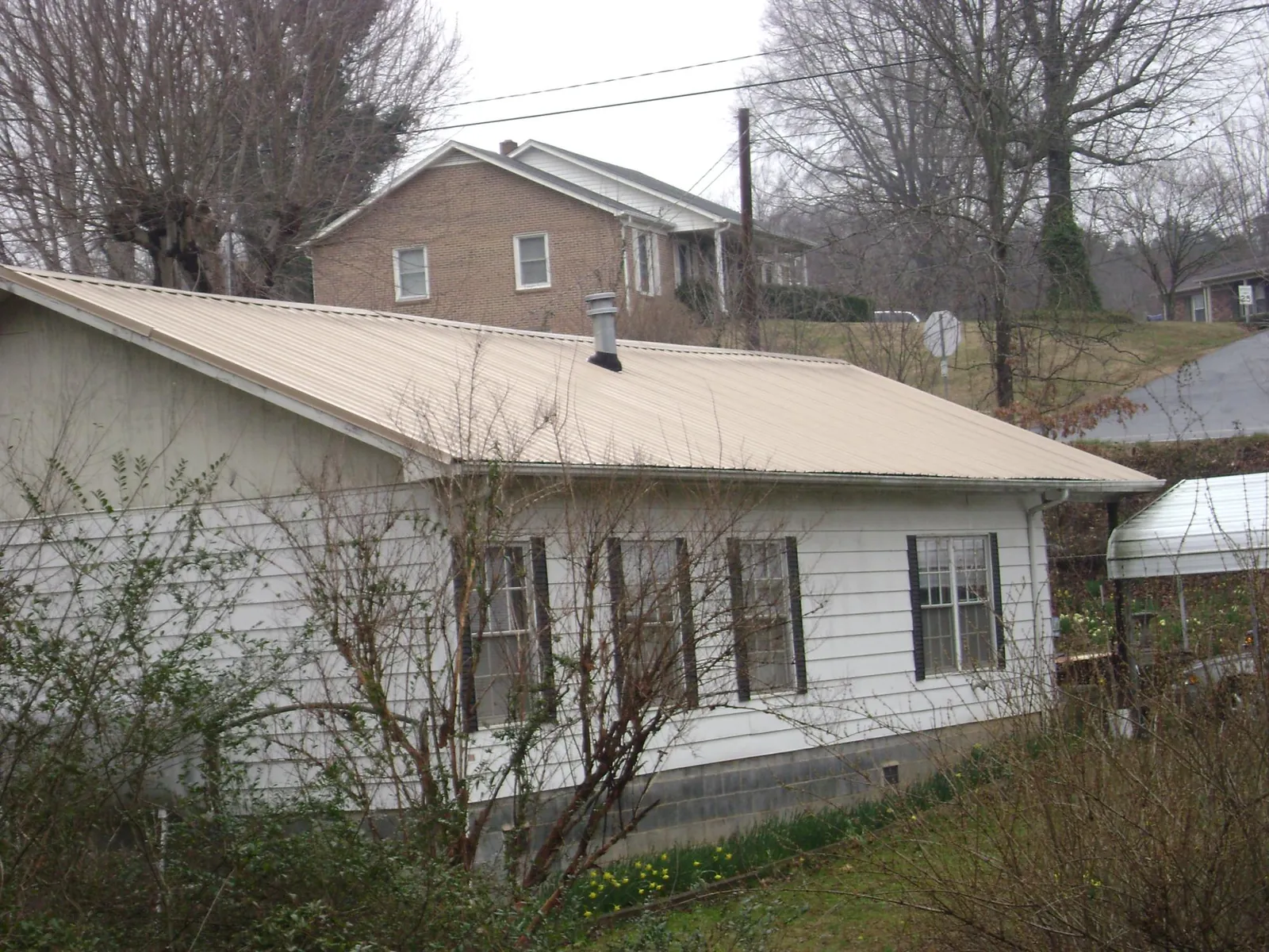 Tan metal roof on a white sided house set into a hillside — Commercial Roofing by Roofing Brothers in Terra Alta