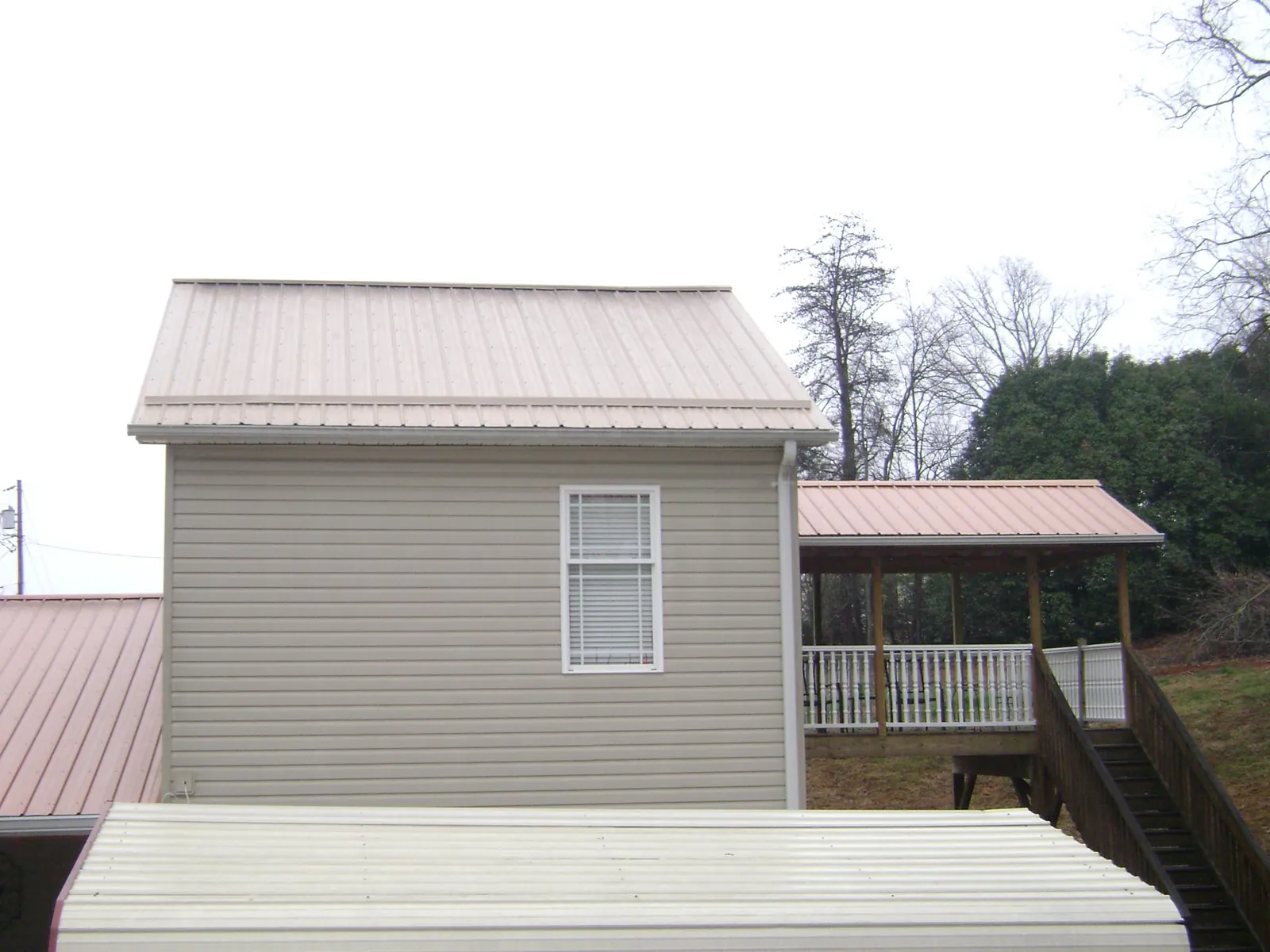 Tan metal roofs on a two story addition and attached porch, from a Roof Replacement job in Terra Alta